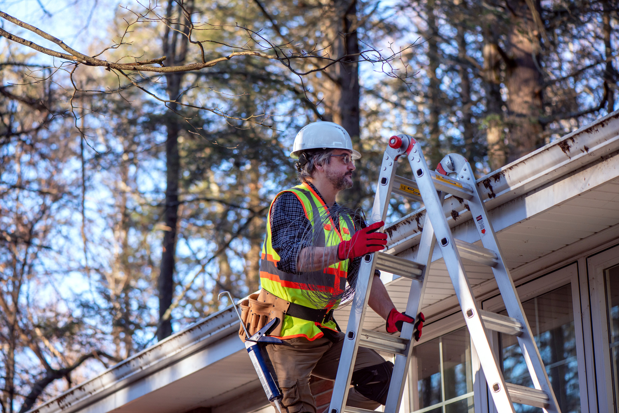 A gutter repair professional getting up on a roof to inspect a gutter system in need of gutter repair in Central Illinois